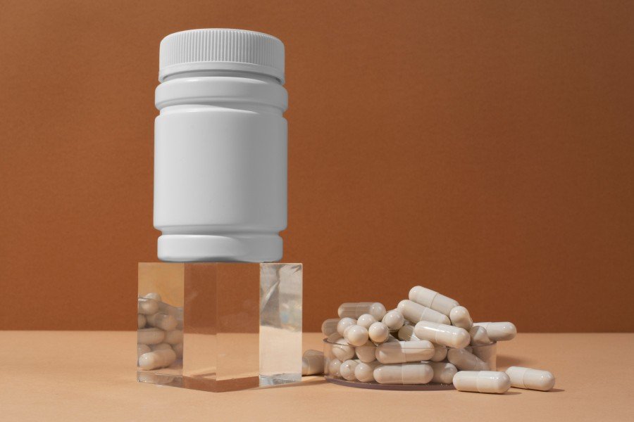 White supplement capsules in a clear container beside a white supplement bottle on a neutral background.