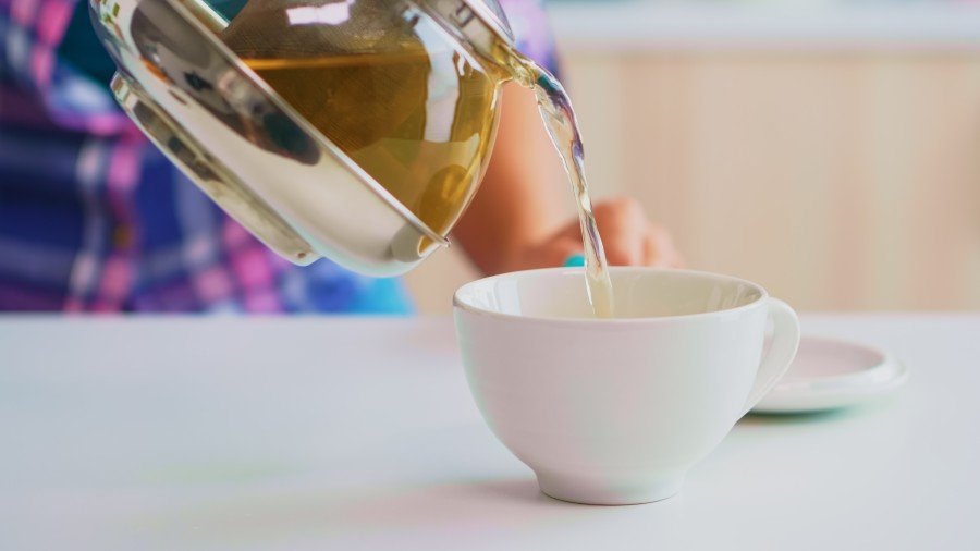 Person pouring jasmine herbal tea from a glass teapot into a white cup