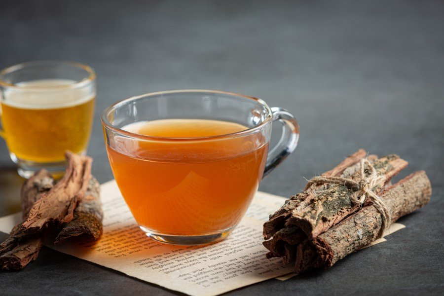 Anti Ageing Infusion Tea brewing in a glass teapot, with a cup of herbal tea and dried flowers on a table.
