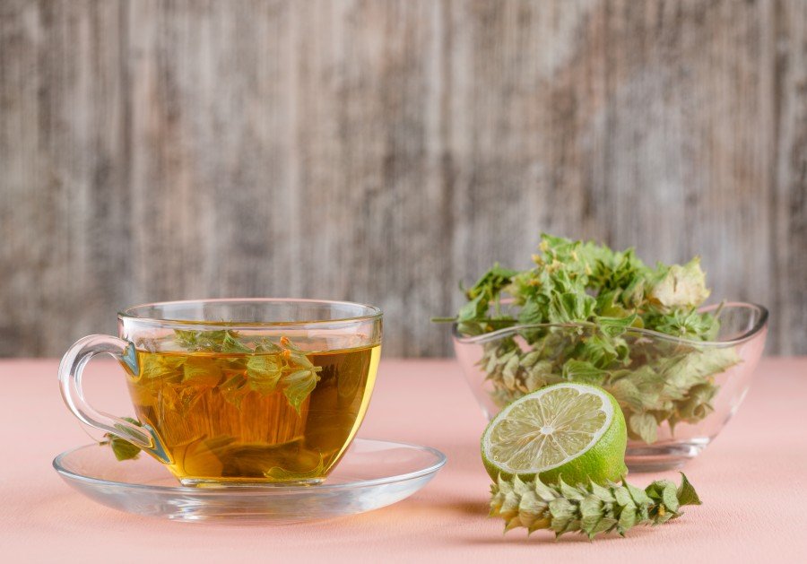 Herbal tea in a glass cup with fresh herbs and lime on a pink table